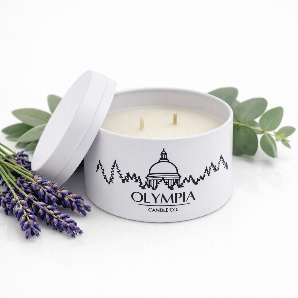 White candle in a tin with 'Olympia Candle Co.' branding, surrounded by lavender and eucalyptus leaves on a white background.