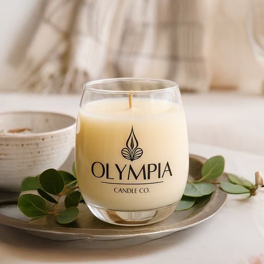 Glass candle with 'Olympia Candle Co.' logo on a decorative plate with green leaves.