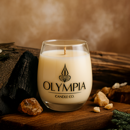 Glass candle with 'Olympia Candle Co.' logo on a wooden surface with natural elements.