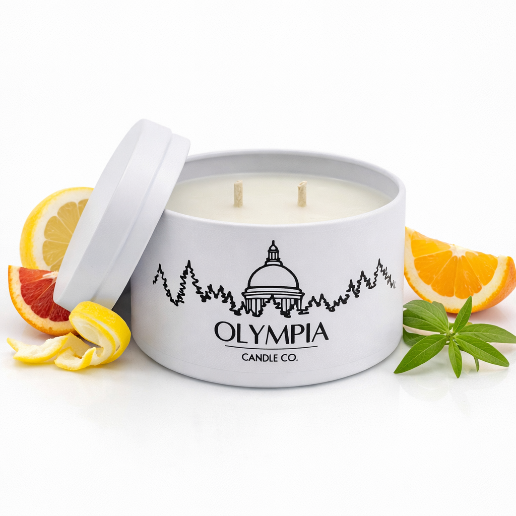 White candle in a tin with 'Olympia Candle Co.' logo, surrounded by citrus fruits on a white background