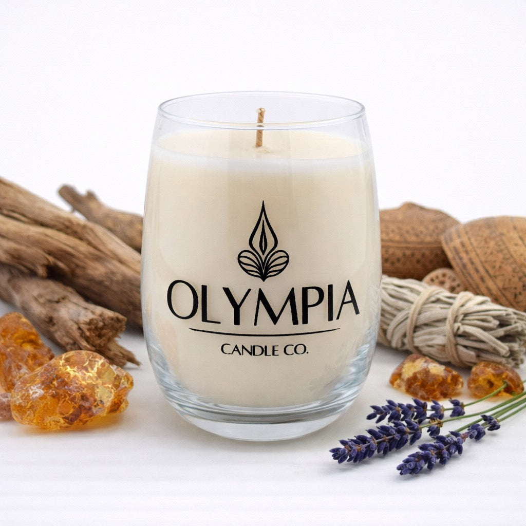 Candle with Olympia Candle Co. branding surrounded by natural elements on a white background