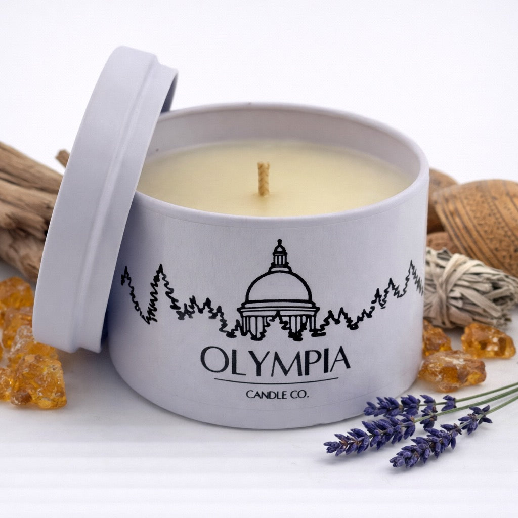 Candle in a white container with 'Olympia Candle Co.' branding, surrounded by decorative elements on a light background.