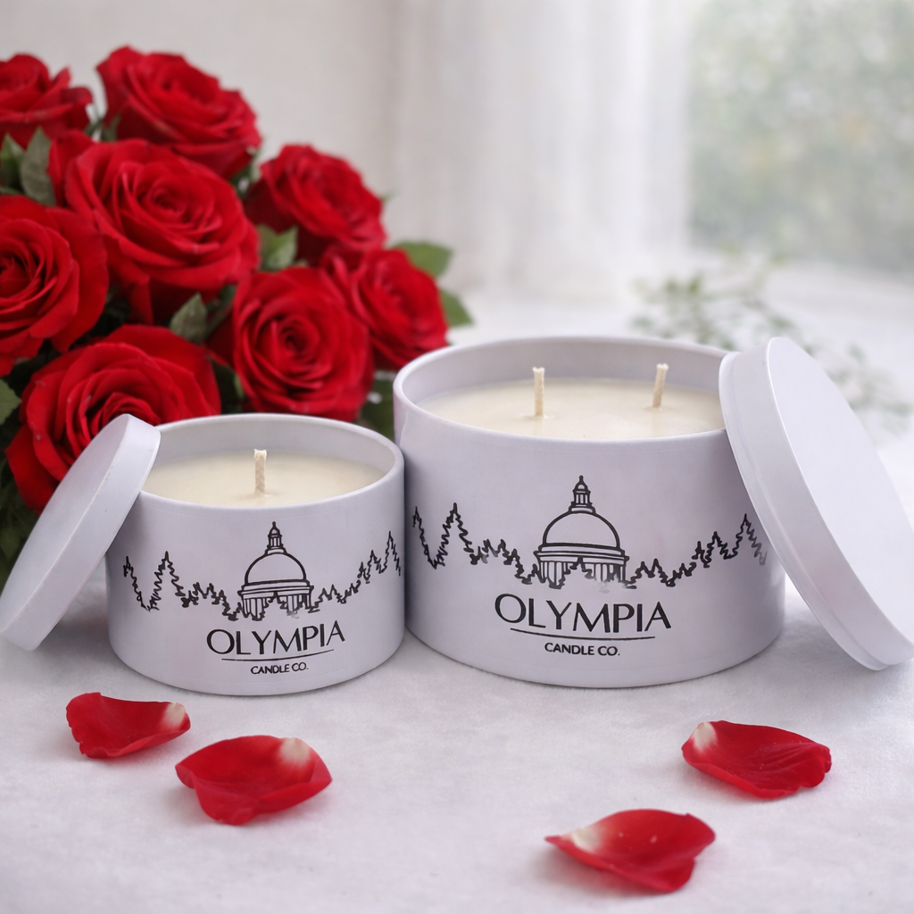 Two Olympia Candle Co candles with red roses and rose petals on a light surface.