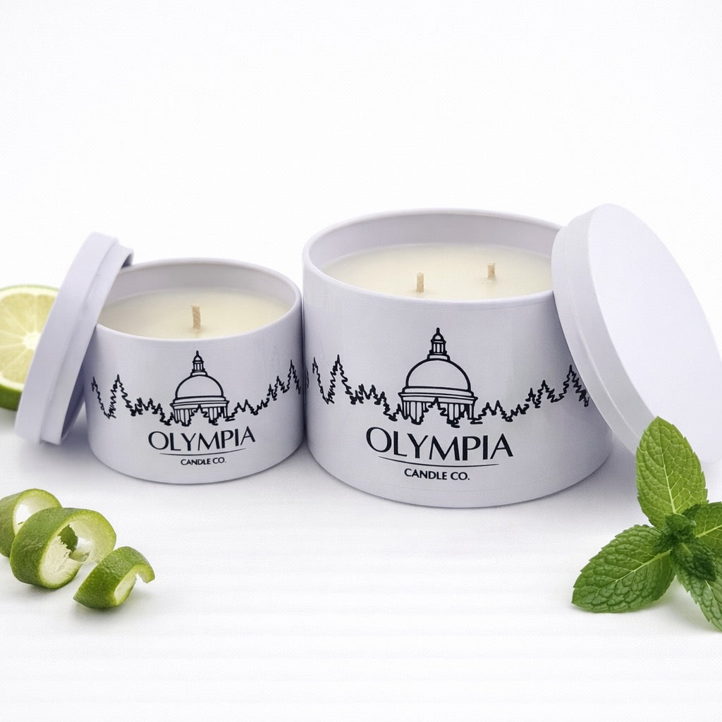 Two Olympia Candle Co. candles in white containers with lime and mint leaves on a white background
